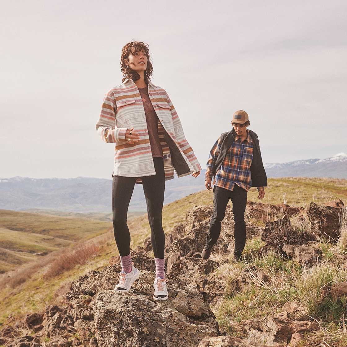 Columbia Two people exploring a rocky hillside with mountains in the background.