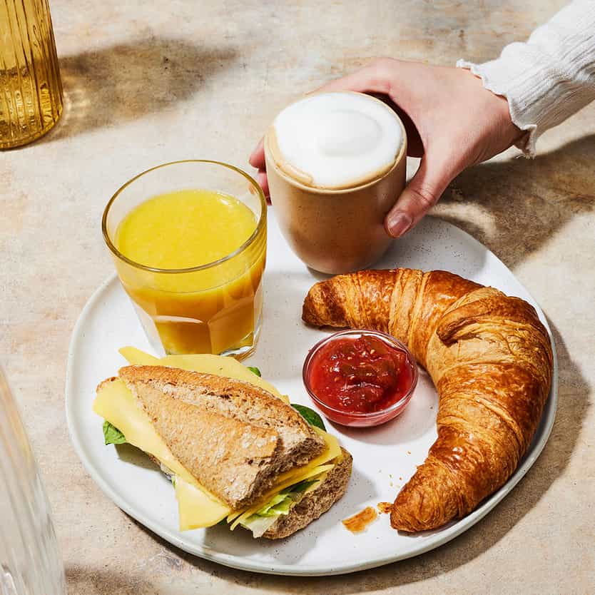 A breakfast situation with juice, cappuccino, sandwich, crossaint and jam