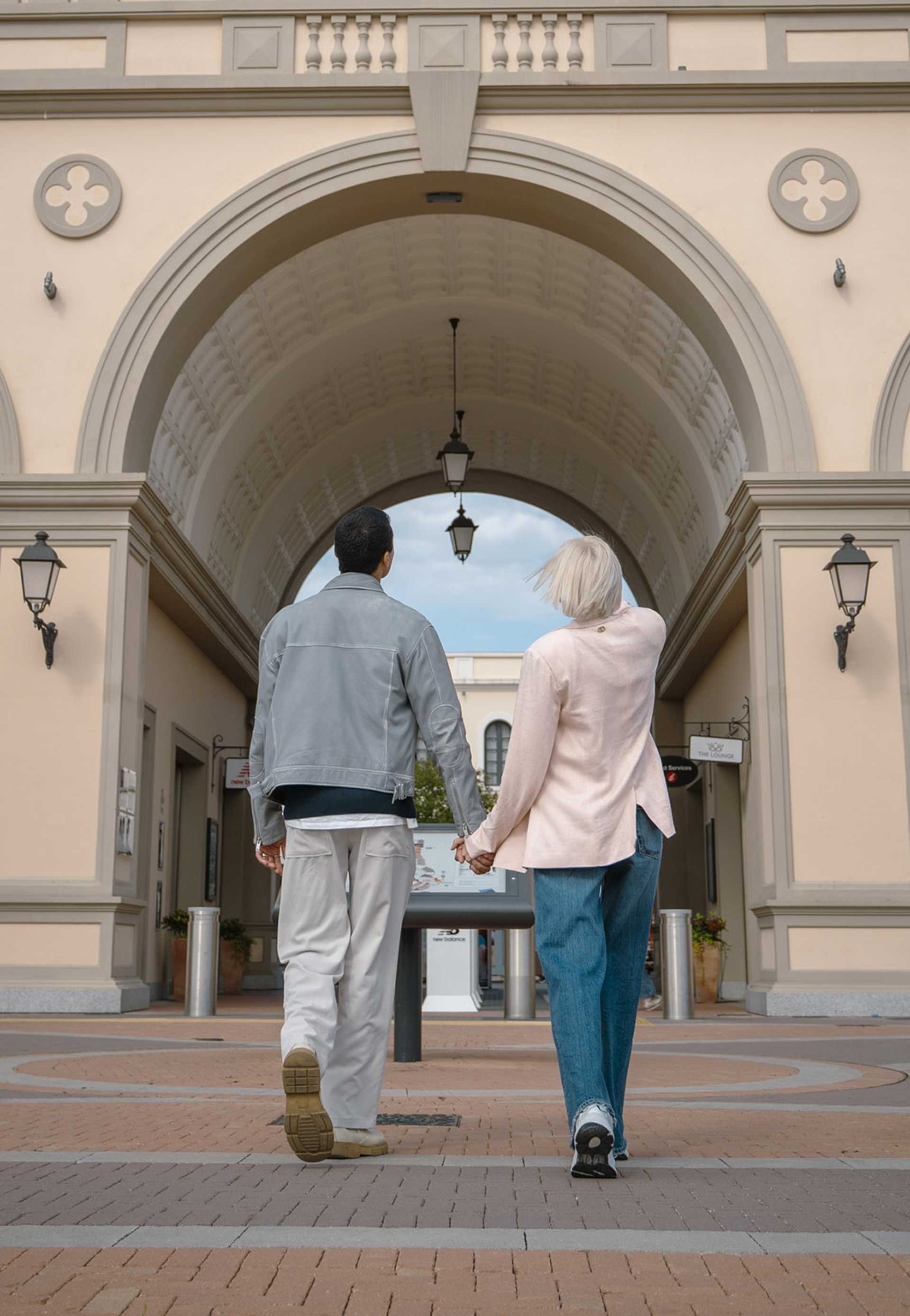A couple walking toward the entrance of Noventa di Piave Designer Outlet, enjoying a sunny day of shopping.
